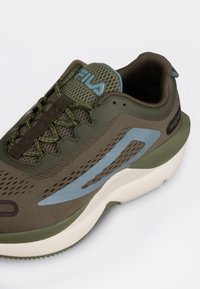 Sneaker atletico marrone con tomaia in rete, accenti blu e una spessa suola bianca. Presenta dettagli testurizzati e lacci verdi.