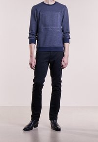 Námořnická pletená mikina s texturovaným čtvercovým vzorem a logem "BOSS ORANGE", doplněná tmavými úzkými kalhotami a černými koženými botami.