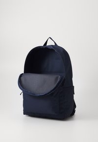 Tamsiai mėlynas audinio kuprinės suapvalinta viršūne, užtrauktuko uždarymu ir priekinė kišenė. Lygus tekstūra, minimalistinis dizainas ir sustiprintas siuvimas.