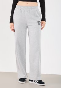 Jasnoszare dresy z elastycznym paskiem w talii, z czarnym napisem "TOKYO 1963", prostymi nogawkami i miękką strukturą materiału.