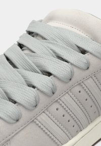 Απαλά γκρι αθλητικά παπούτσια με λεία υφή, που διαθέτουν επίπεδους κορδόνια με υφή, διάτρητες λεπτομέρειες και διακριτικές οριζόντιες ρίγες στις πλευρές.