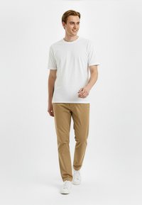 T-shirt blanc à manches courtes, pantalon beige et baskets blanches. La tenue présente une coupe décontractée avec un encolure classique et un design minimaliste.
