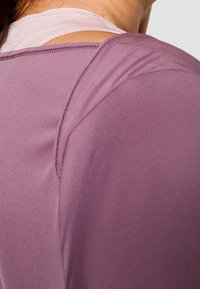 Top sportivo viola con tessuto morbido e elastico. Presenta un collo a barca e un design sovrapposto con spalline chiare visibili sul retro.