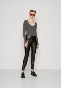 Gray long-sleeve fitted top with a scoop neckline, paired with high-waisted black faux leather pants. Black platform shoes complete the look.
