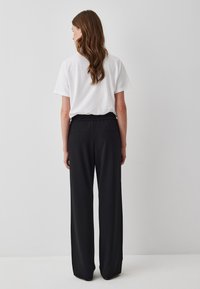 Witte katoenen t-shirt met korte mouwen, gecombineerd met zwarte wijde broek met elastische tailleband en twee achterzakken.