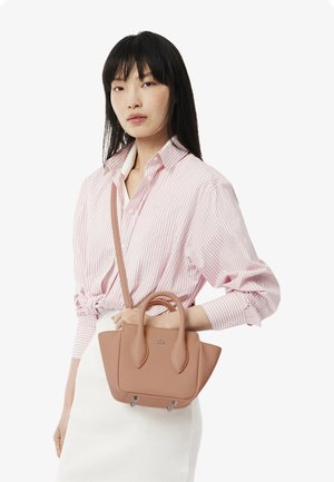 Braune Lederhandtasche mit abgerundeten Seiten, doppelten Griffen, verstellbarem Riemen und silbernen Hardware-Akzenten. Getragen mit einem rosa gestreiften Hemd.