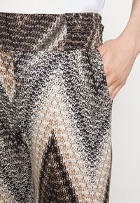 Hlače z vzorcem v mešanici rjave, črne in smetanaste barve. Elastičen pas s stranskimi žepi in mehak, teksturiran material.