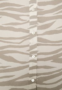Beige skjorta med ett zebramönster i ljusbrunt. Den har vita knappar som löper ner längs framsidan och en mjuk tygkänsla.