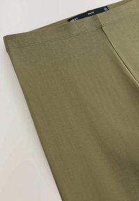 Maslinasto zelene, lagane, rastezljive tajice s glatkom teksturom. Imaju jednostavan dizajn i crnu oznaku branda na pojasu.