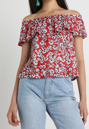 Haut rouge épaules dénudées avec manches à volants ornées d'un motif floral en noir et blanc. Associé à un jean taille haute bleu clair.