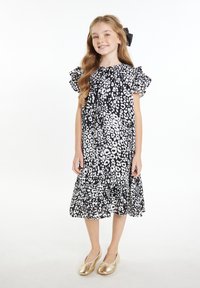 Schwarzes und weißes Blumenmuster-Kleid mit Rüschensleeves und ausgestelltem Saum. Kombiniert mit goldenen Slippern. Glatte Stoffoberfläche.