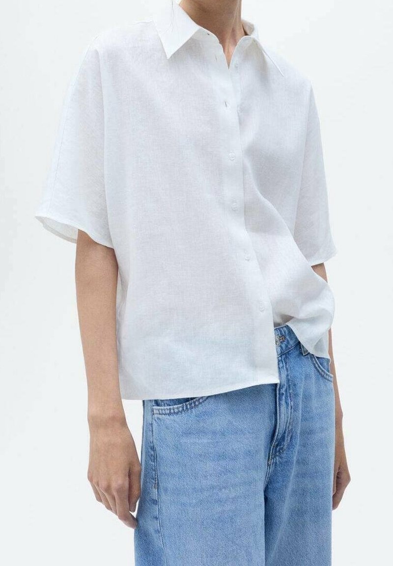 Camisa de lino blanca de manga corta con cuello puntiagudo y cierre de botones, combinada con unos vaqueros de tiro alto en azul claro. Diseño simple y limpio.