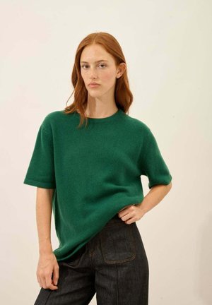 Maglione verde a maglia a maniche corte con colletto rotondo, abbinato a jeans scuri a vita alta. Tessuto morbido, vestibilità casual e design minimal.