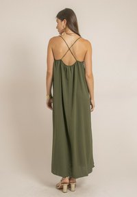 Robe maxi en vert olive, avec des bretelles fines et réglables, une coupe ample et un dos froncé. Tissu lisse, silhouette longue jusqu'au sol et éclat subtil.