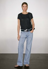 Zwarte t-shirt met korte mouwen van lichtgewicht stof, gecombineerd met lichtblauwe wijde jeans, en afgewerkt met een zwarte riem met een zilveren gesp.