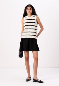Haut sans manches en tricot crème avec des rayures horizontales noires, associé à une jupe noire évasée et des ballerines noires avec des clous. Petit sac à main noir.