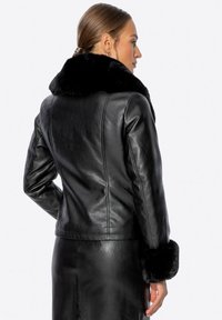 Černá kožená bunda s měkkým černým kožíškem z umělé kožešiny na límci a manžetách. Má přiléhavý střih a hladkou strukturu. Čistý silueta s detaily švů.