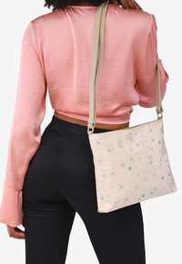 Borsa a tracolla beige con ricami floreali in blu e verde. Materiale in pelle liscia, forma rettangolare e tracolla regolabile.