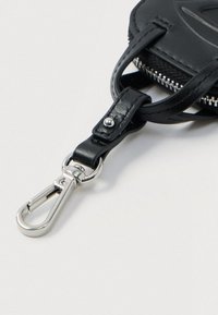 Μαύρη δερμάτινη θηλιά για κλειδιά με ασημένια μεταλλική κλείστρα που είναι συνδεδεμένη με μια μαύρη τσάντα με φερμουάρ σε άσπρο φόντο.