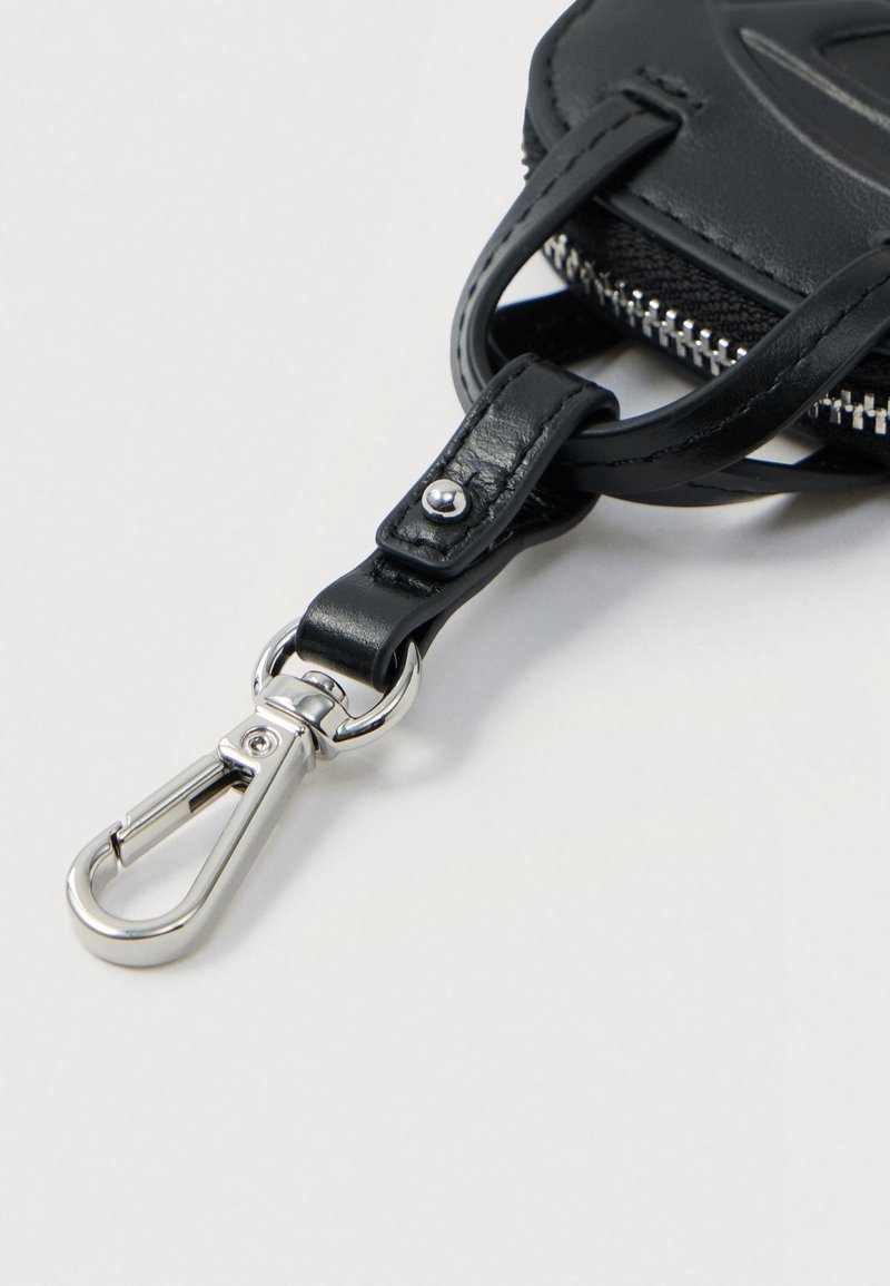 Sangle de porte-clés en cuir noir avec un fermoir en métal argenté attaché à une pochette zippée noire sur fond blanc.