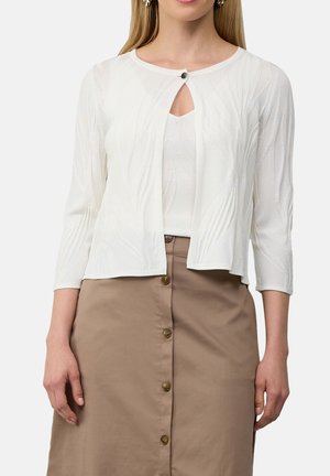 Witte cardigan met lange mouwen, voorzien van een gestructureerd bladerenpatroon en een sluiting aan de voorkant met een zwarte knop; gedragen over een aansluitend topje en rok.