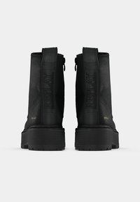 Bottines noires avec une surface texturée, présentant un logo prominent sur le côté, une semelle en caoutchouc épaisse et des fermetures éclair à l'arrière.