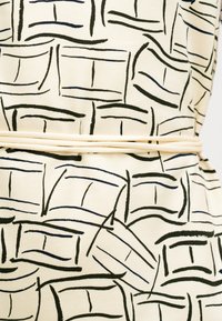 Ύφασμα σε κρεμ χρώμα με μαύρο αφηρημένο μοτίβο από γραμμές και σχήματα. Μια λεπτή μπεζ ζώνη περιβάλλει τη μέση στο κέντρο.