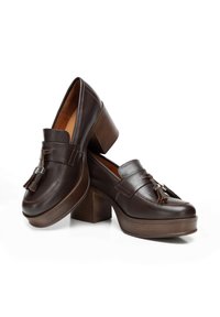Braune Lederloafer mit blockhaftem Absatz, ausgestattet mit einem dekorativen Quaste und metallischem Akzent. Glatte Textur und klassische Designelemente.