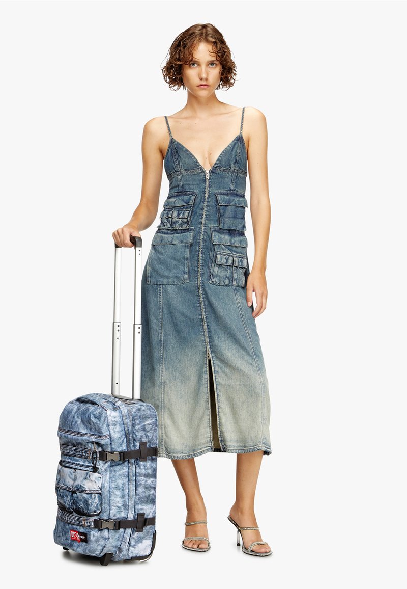 Vestido de denim con tirantes delgados y cremallera frontal, con bolsillos parche; la maleta que lo acompaña tiene un patrón de tie-dye azul y correas ajustables.