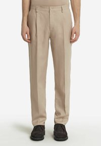 Beige byxor med en lös passform, texturerat tyg, framfållar, bältesöglor och en enda knappstängning. Svarta skor fulländar outfiten.