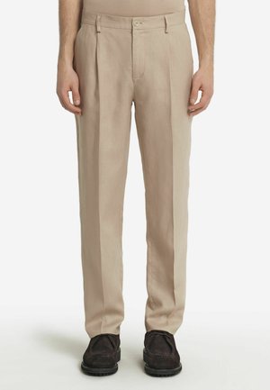 Beige byxor med en lös passform, texturerat tyg, framfållar, bältesöglor och en enda knappstängning. Svarta skor fulländar outfiten.