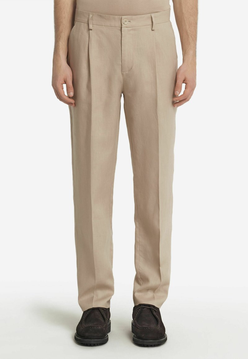 Beige byxor med en lös passform, texturerat tyg, framfållar, bältesöglor och en enda knappstängning. Svarta skor fulländar outfiten.