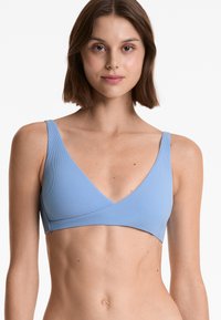 Ljusblå ribbad bralette med breda axelband, V-ringning och korsdesign; slät textur och figurnära silhuett.