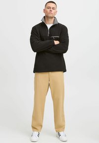 Black fleece pullover with gray collar, half-zip, and front pocket. Beige pants and white sneakers with black stripes. Smooth texture.