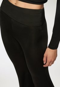 Leggings neri con vita alta e texture liscia, dal design aderente e dettagli delle cuciture sottili. Il tessuto è elegante ed elastico.