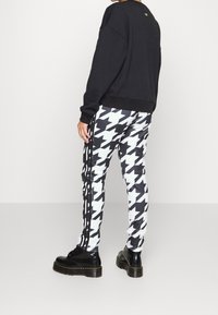 Černá mikina s vroubkovaným lemem, kombinovaná s kalhotami v kostkovaném vzoru černobílé houndstooth, které mají černé pruhy, a robustními černými botami.