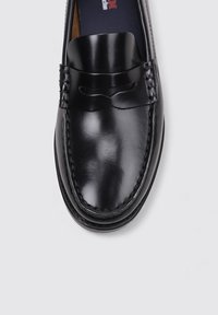 Mocasines de cuero negro con acabado liso, detalles de costura alrededor de los bordes y un adorno decorativo en la parte frontal. Suela plana diseñada para la comodidad.