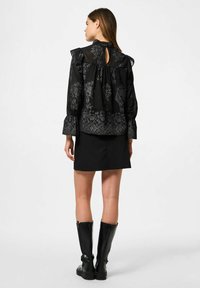 Blusa nera con motivo floreale, spalle arruffate e schiena a chiave, abbinata a una gonna nera e stivali neri fino al ginocchio.