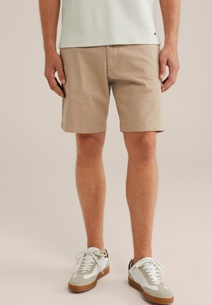 Beige Baumwollshorts mit umgeschlagenen Säumen, kombiniert mit weißen Sneakers mit grauen Akzenten und braunen Sohlen. Einfaches Design, geeignet für die Freizeit.