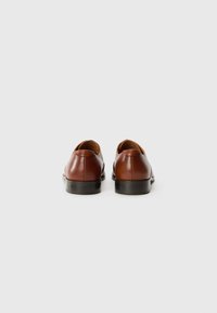 Zapatos de cuero marrón con un acabado suave, punta redonda, tacón bajo negro y sutiles detalles de costura en la parte trasera y los laterales.