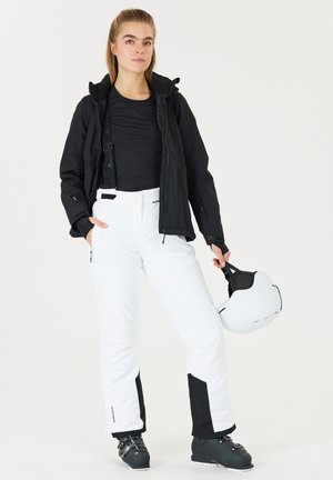 Ski outfit featuring a black waterproof jacket, fitted black shirt, white snow pants with black accents, and black ski boots. Includes a white helmet.