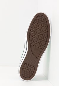 Brown rubber shoe sole with a textured geometric pattern, white edges, and a Converse logo. The shoe leans against a white background.