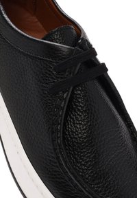 Scarpa in pelle nera con finitura testurizzata, suola in gomma bianca e lacci neri. Presenta una punta rotonda e un design minimalista.