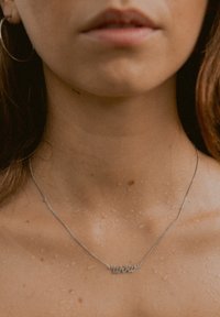Silberkette mit "Wow" Anhänger, zarte Kette, die auf nasser Haut ruht und feine Details sowie eine glatte Textur zeigt.