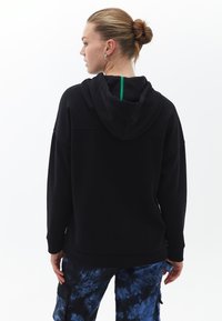 Felpa nera con cappuccio e interno morbido, caratterizzata da una zip verde. Abbinata a pantaloni cargo blu tie-dye, con una vestibilità rilassata.