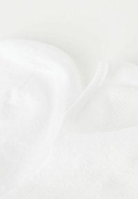 Vita bomullssockor med ribbad textur vid kanten och slät yta, som visar överlappande tygskikt och sömlös design.