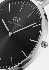 Black dial watch with silver hour markers and hands, stainless steel case, and crown. Features a minimalist design with a sleek finish.