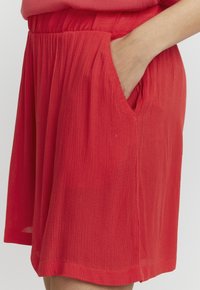 Shorts rouges en tissu léger et texturé, dotés d'une taille élastique et de poches latérales, avec une coupe ample et une longueur au-dessus du genou.