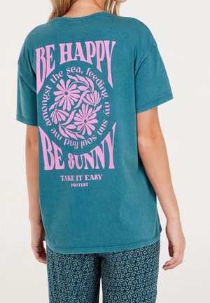T-shirt bawełniany w kolorze morskim z dużym różowym napisem na plecach: "BĄDŹ SZCZĘŚLIWY" i "BĄDŹ SŁONECZNY", ozdobiony kwiecistym wzorem graficznym. Krótkie rękawy, luźny krój.