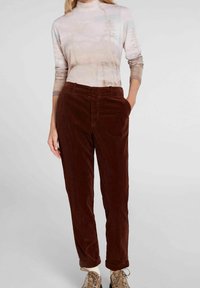 Ruskeat pellavahousut suoran fitin kanssa, joissa on sivutaskut ja hienostunut tekstuuri. Yhdistetty kevyen, kuviollisen pitkähihainen paidan kanssa.